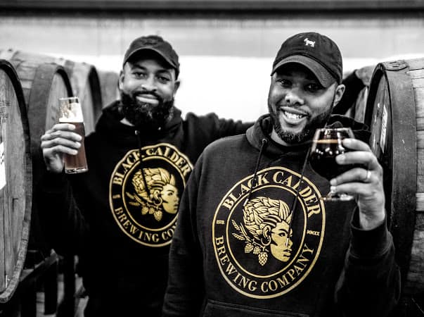 owners Zachary Rostic and Jamaal Ewing pose with Black Clader logo sweatshirts and brews